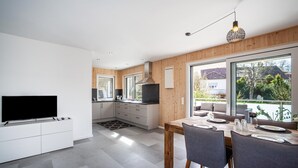 A modern kitchen with a TV, wooden cabinets, and a dining area with a table set for two. - Holiday Apartment 'Wohnen an der Ach' with Private Garden, Balcony and Wi-Fi (Bad Wurzach)