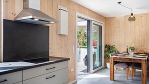 A modern kitchen with wooden paneling, a black countertop, and a dining area with a wooden table and chairs. - Holiday Apartment 'Wohnen an der Ach' with Private Garden, Balcony and Wi-Fi (Bad Wurzach)