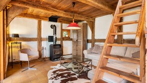 Um interior rústico com teto de madeira, mesa de centro de vidro, sofá, escada e lareira.