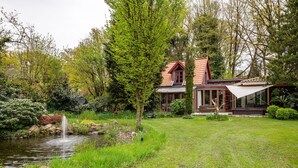 Uma casa com um lago, rodeada por vegetação exuberante e árvores.