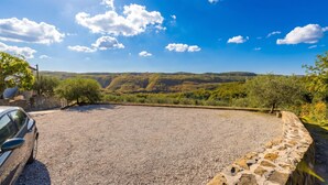 A gravel parking area with a stone wall, a parked car, and a view of rolling hills under a clear sky. - Tourist Farm Tonin Apartments (Koper)