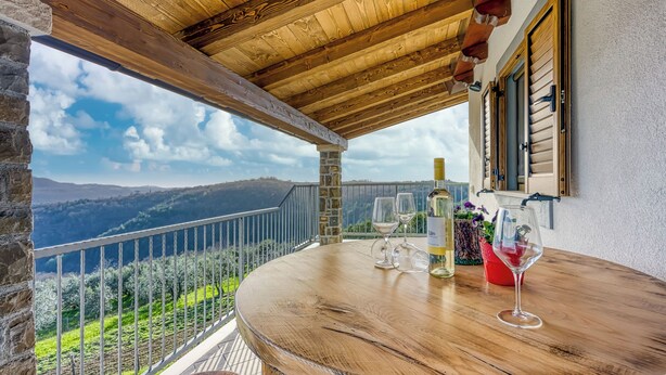 A wooden balcony with a view of mountains, a table with wine glasses, and a bottle of wine. - Tourist Farm Tonin Apartments (Koper)