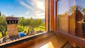 A room with a large window, a stone fireplace, and a view of a green landscape. - Tourist Farm Tonin Apartments (Koper)