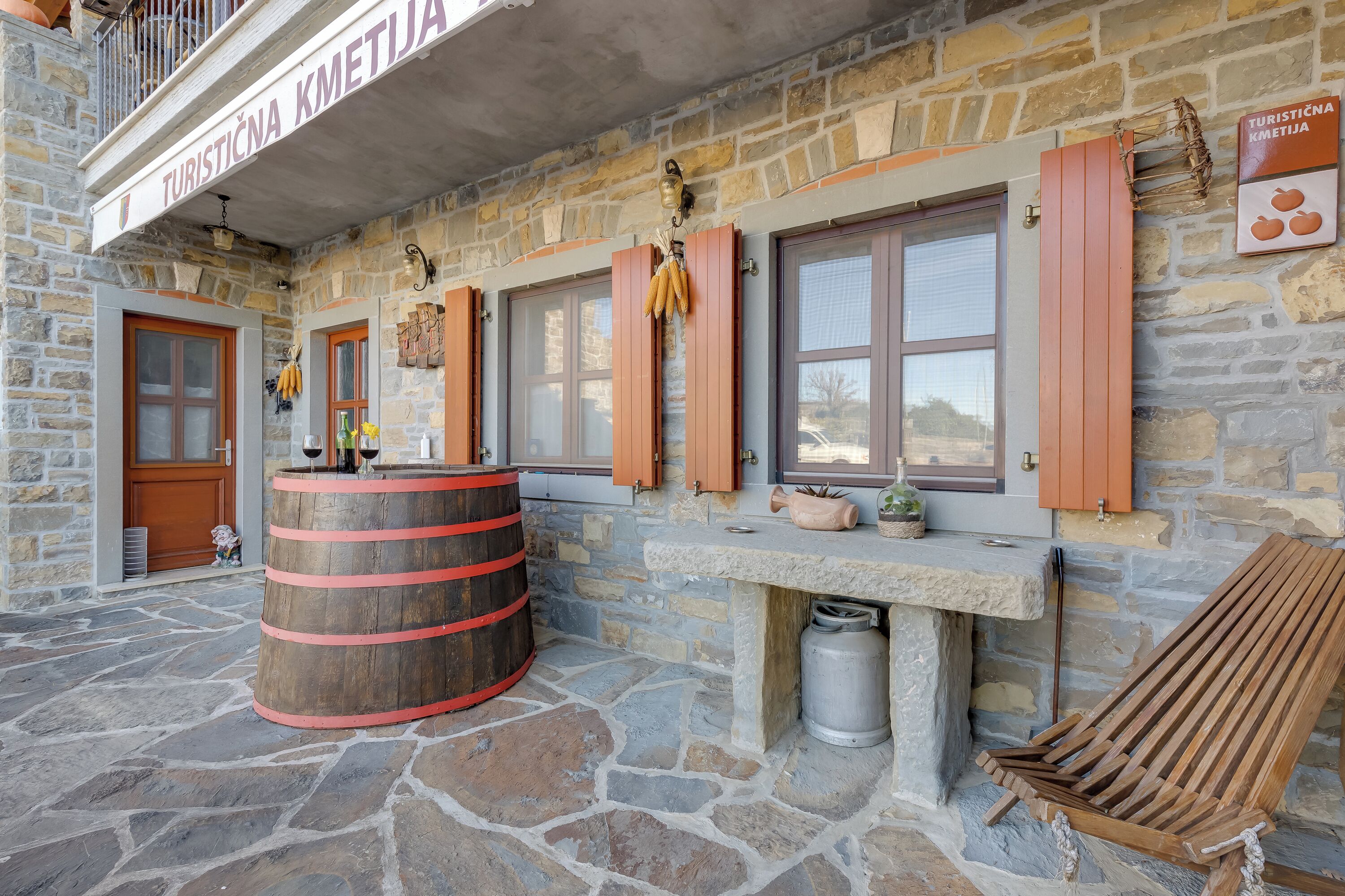 Un bâtiment en pierre avec une enseigne indiquant « Turistična Kmetija ». On y trouve un tonneau en bois, un banc et une fenêtre avec des volets.