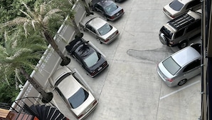 Vista aérea de un estacionamiento con varios autos estacionados en filas, rodeado de árboles y un edificio.