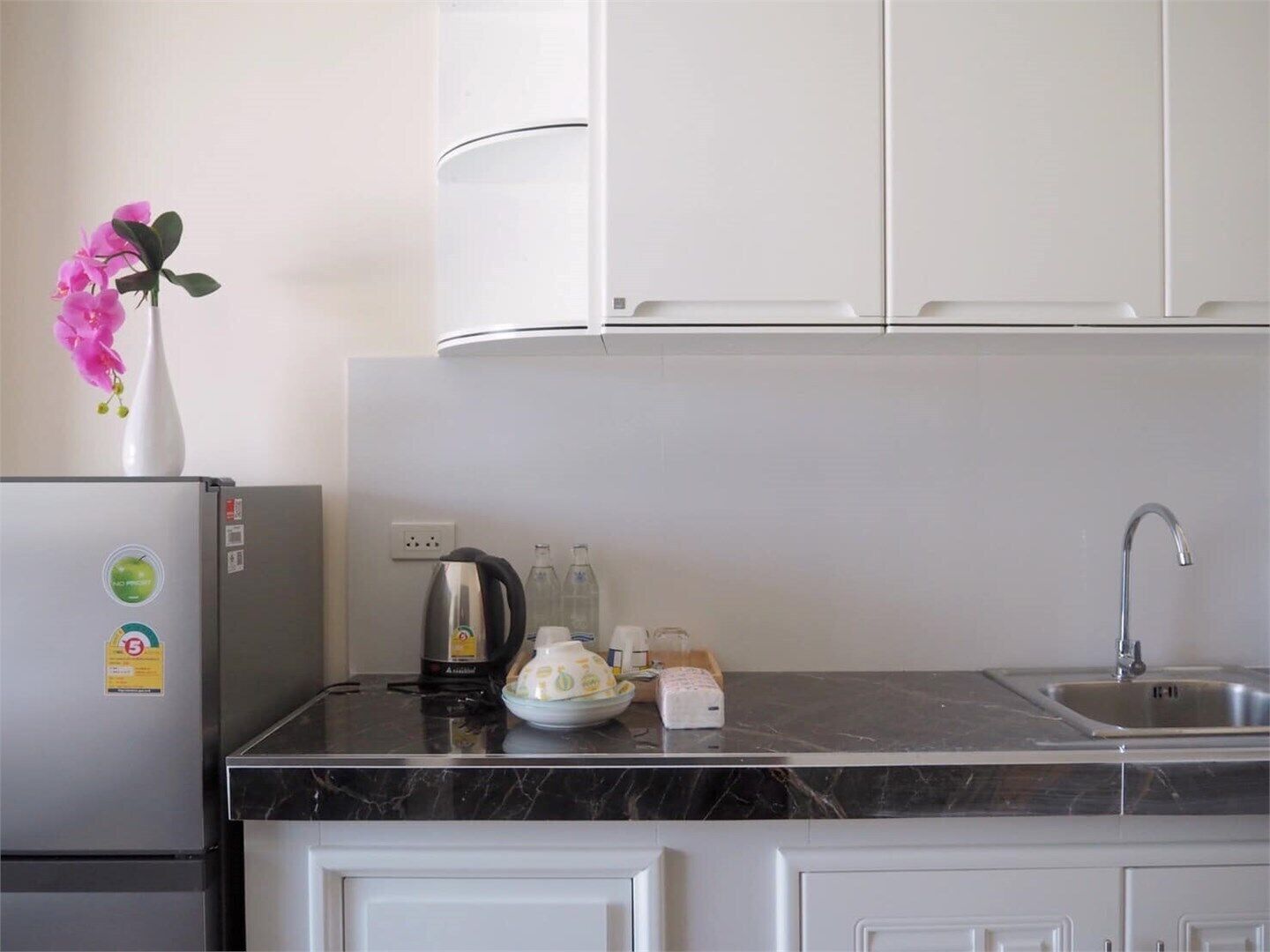 A kitchen with white cabinets, a marble countertop, a refrigerator, a sink, and a vase with flowers.
