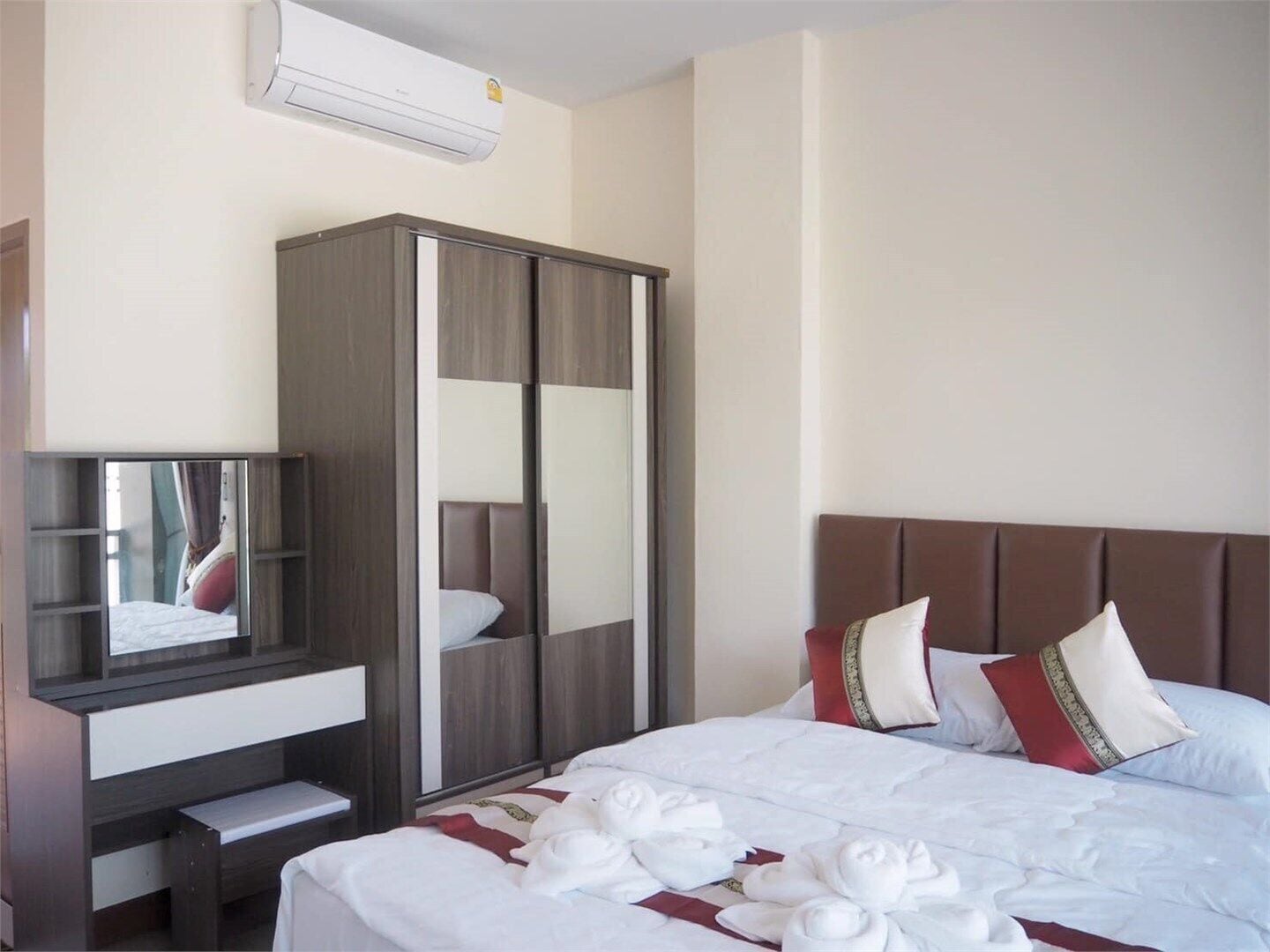 Una habitación de hotel con cama, armario, escritorio con espejo y equipo de aire acondicionado.