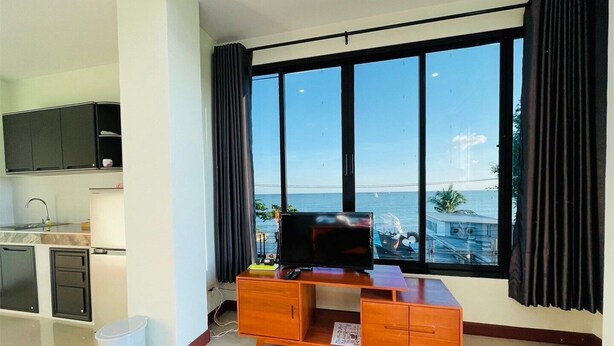 Una sala de estar moderna con un ventanal grande, un escritorio de madera, un televisor y una zona de cocina.