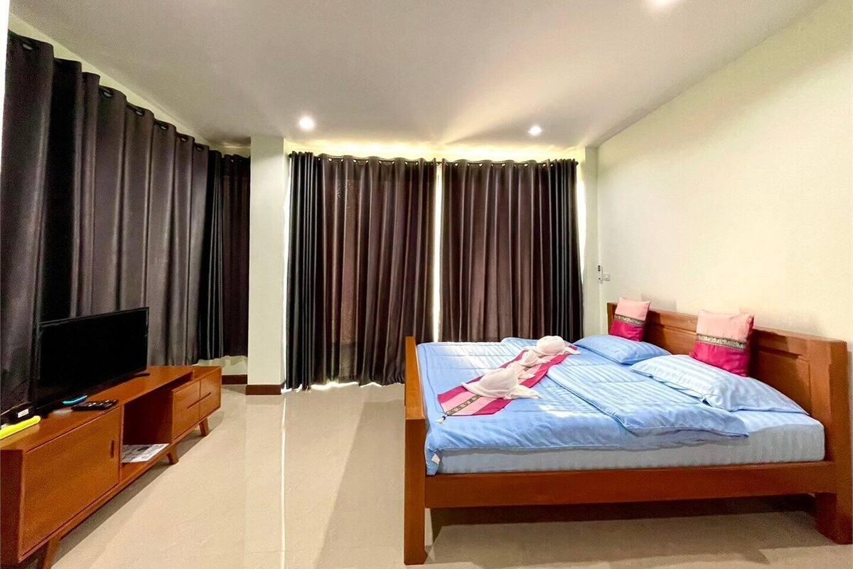 A hotel room with a bed, a TV on a wooden stand, and dark curtains.