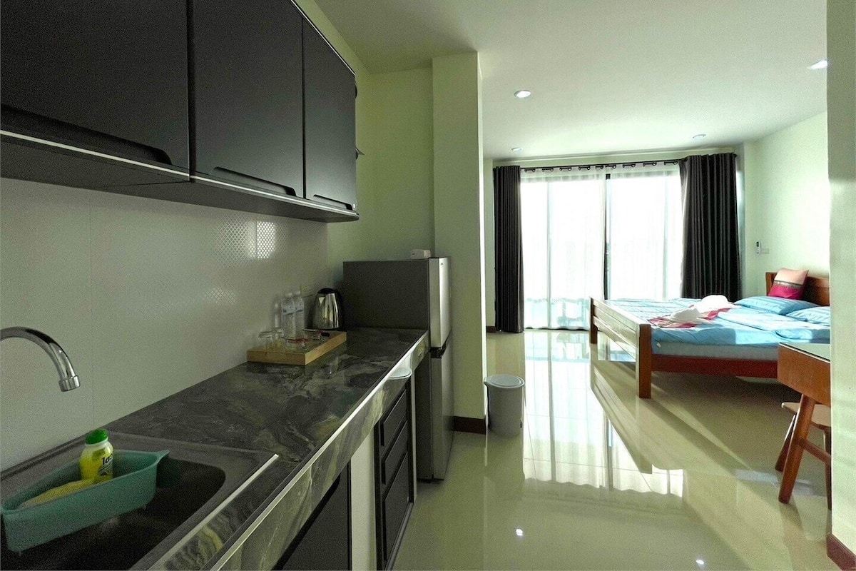 A modern hotel room with a kitchen area, a bed, and a bathroom.