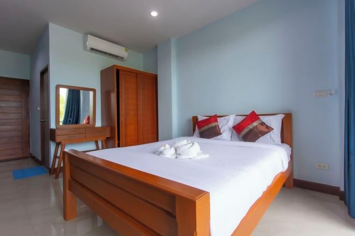 A bedroom with a wooden bed, a wardrobe, a mirror, and an air conditioning unit.