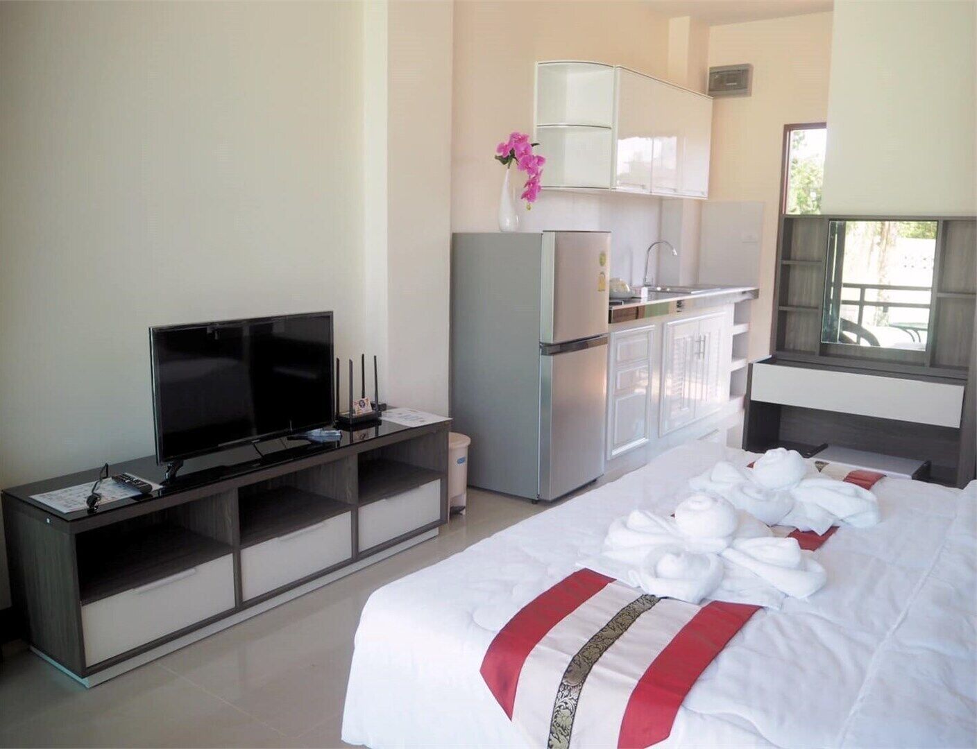 A hotel room with a bed, a TV, a kitchenette, and a window.