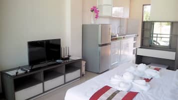 A hotel room with a bed, a TV, a kitchenette, and a window.