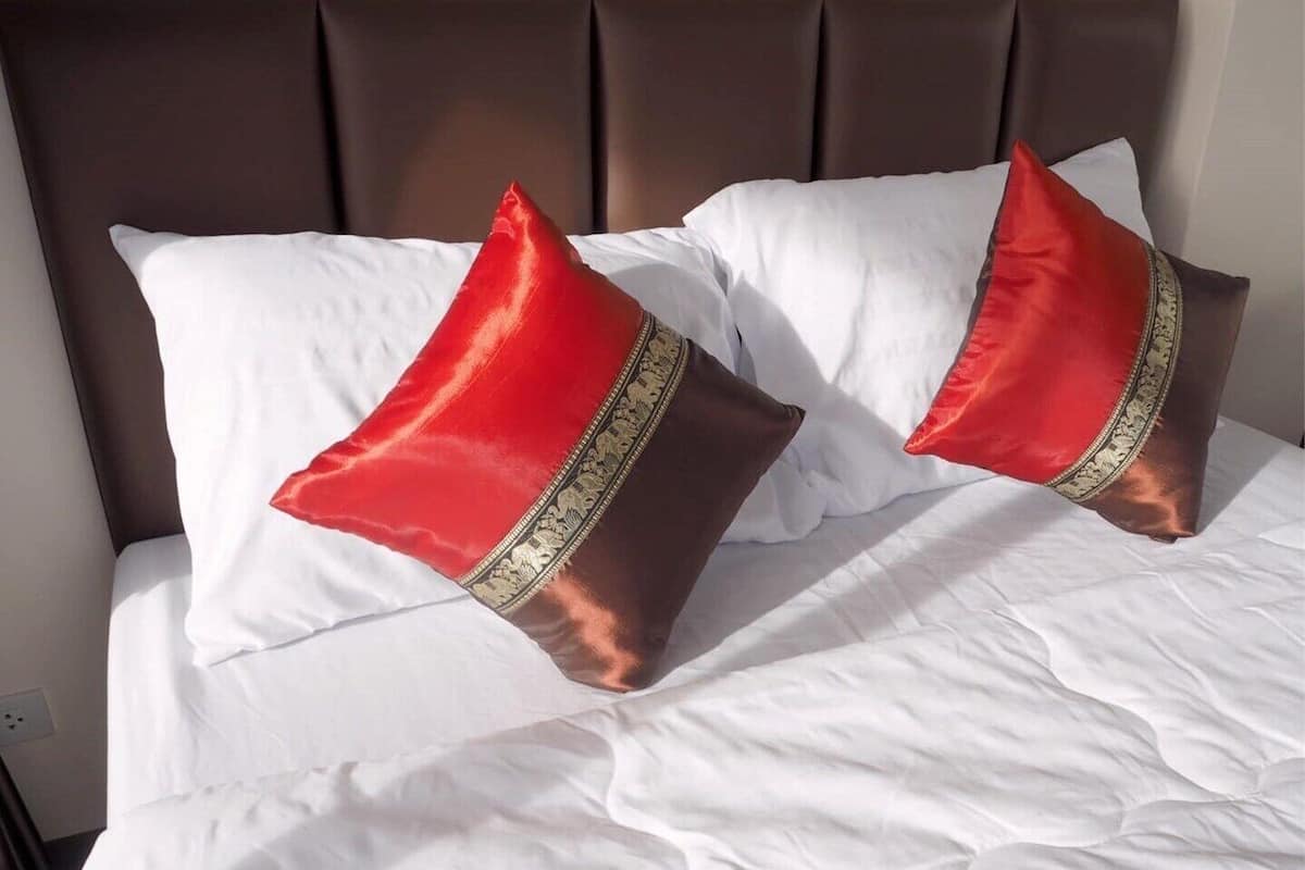 A bed with white linens and two red pillows with gold trim.