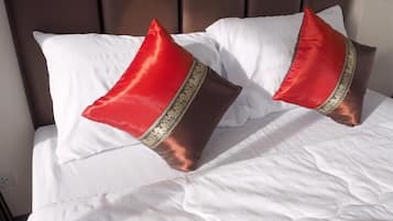 A bed with white linens and two red pillows with gold trim.