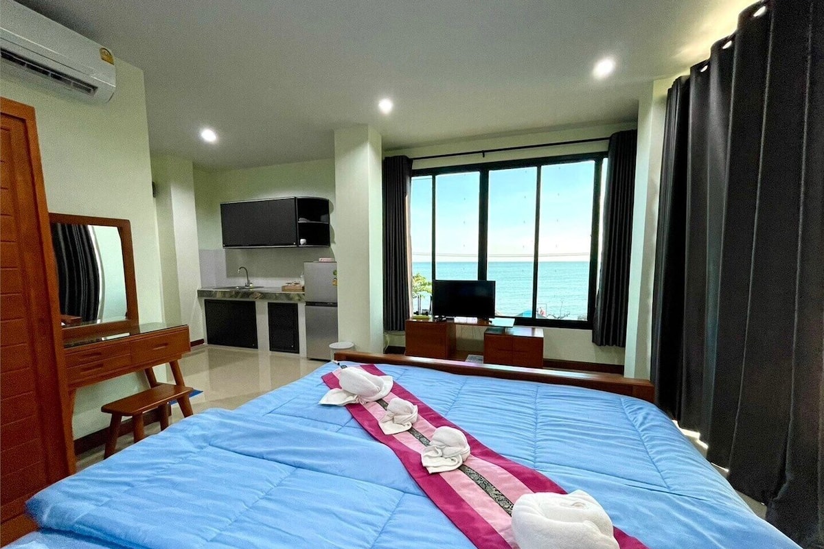 A hotel room with a bed, a desk, a television, and a view of the sea.