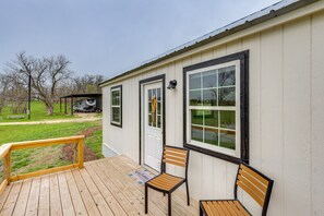 A wooden deck with two chairs and a welcome mat outside a building with large windows and a door.