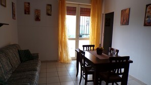 A room with a sofa, a dining table with chairs, a window with curtains, and wall-mounted artwork.