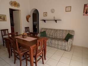 Un área de comedor con una mesa y sillas de madera, un sofá estampado y un espejo en la pared.