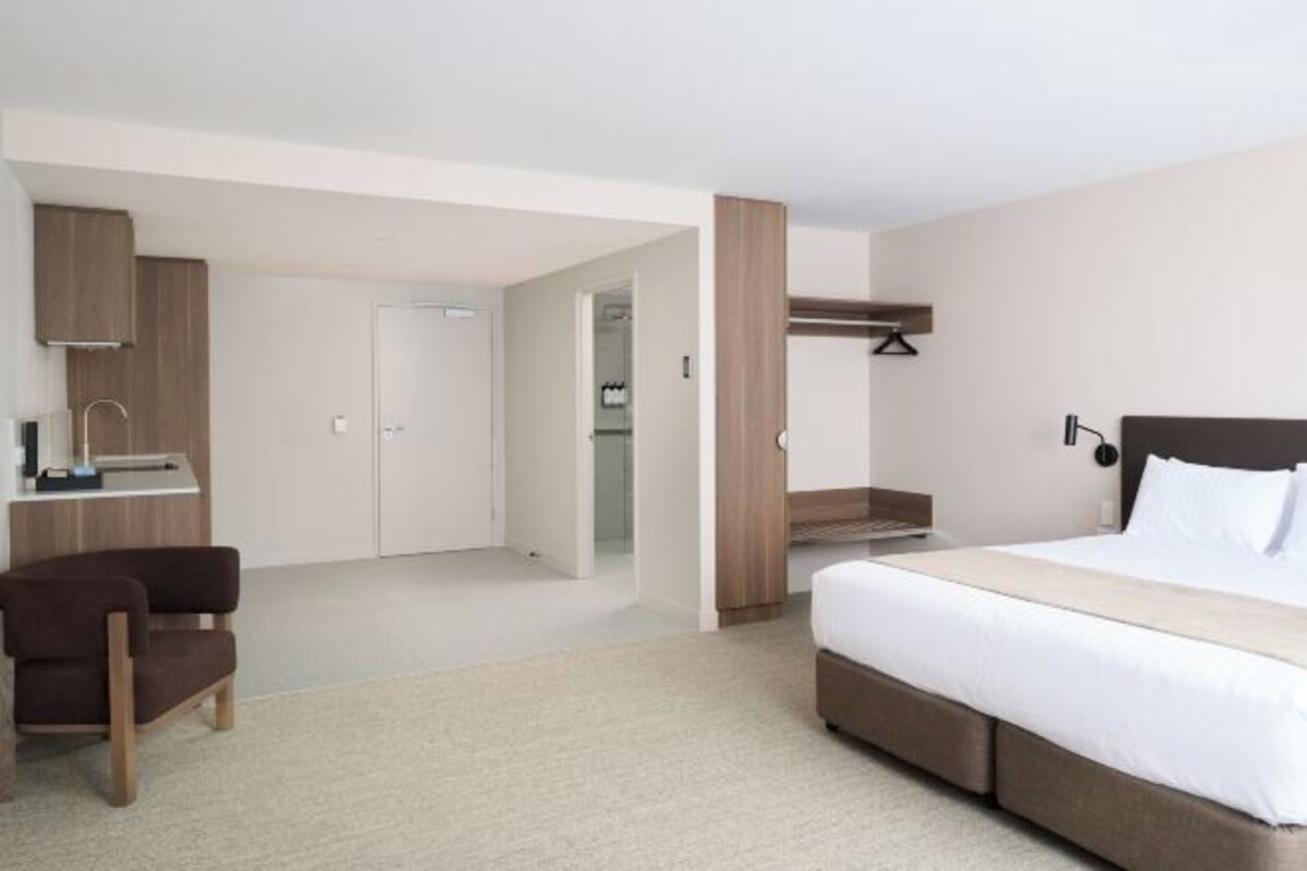 A modern hotel room with a large bed, a desk, a chair, and a bathroom visible through an open door.