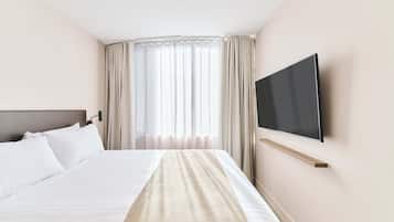 Ein Hotelzimmer mit einem Bett, einem an der Wand montierten Fernseher und einem Fenster mit Vorhängen.