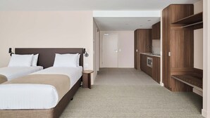 A hotel room with two beds, a wooden wardrobe, a built-in oven, and a small bedside table.