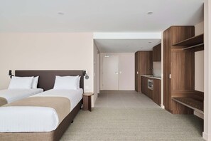 A hotel room with two beds, a wooden wardrobe, a built-in oven, and a small bedside table.