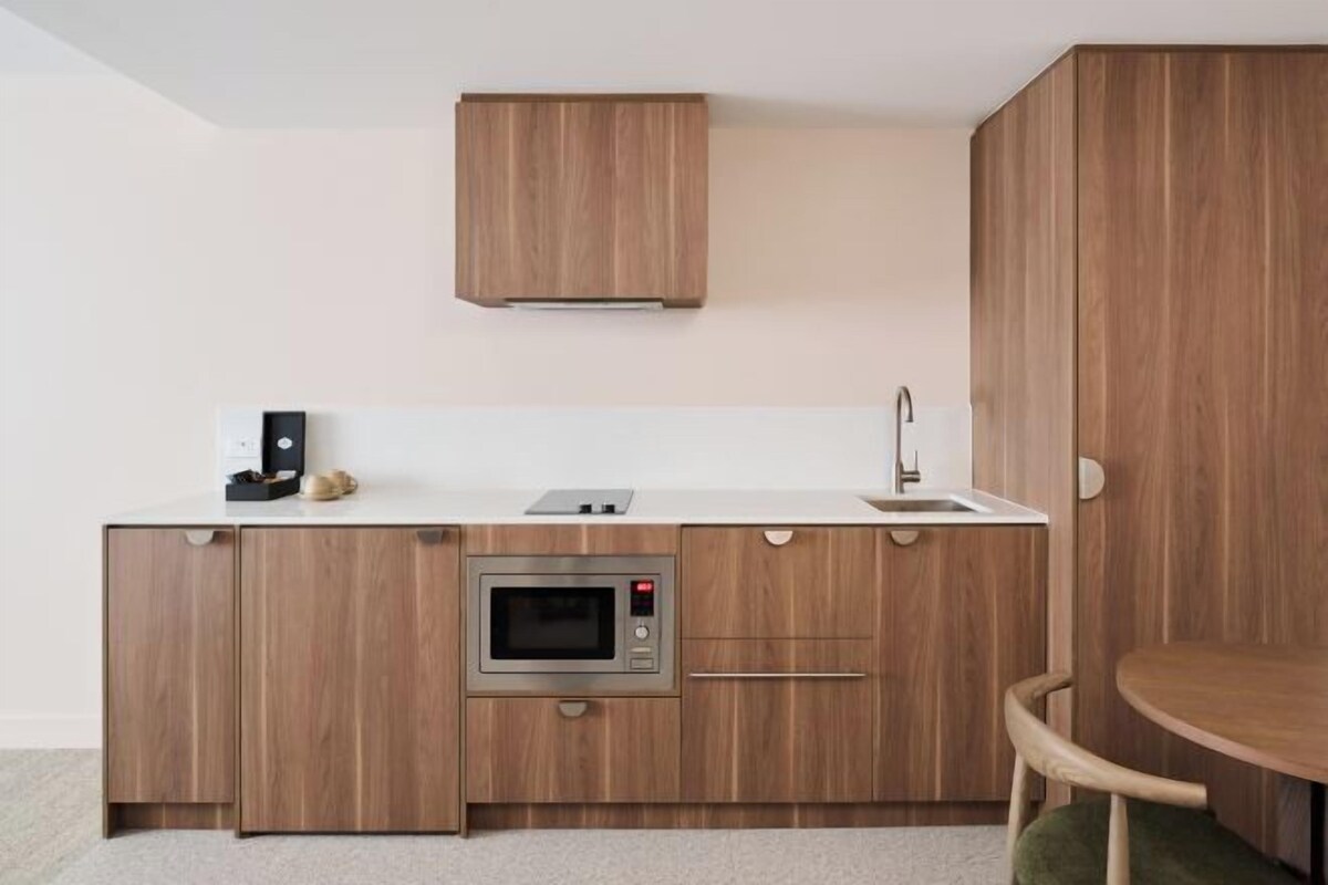 A modern kitchen with wooden cabinetry, a built-in oven, a sink, and a small countertop with a coffee maker and a toaster.