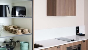 A modern kitchen with a white countertop, wooden cabinets, and a built-in oven. There are shelves with kitchenware and a coffee maker. - Abode Phillip (Phillip)