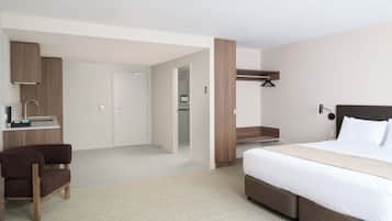 Ein modernes Hotelzimmer mit einem Bett, einem Schreibtisch mit Stuhl, einem Kleiderschrank und einem durchgegangenen Tür einsehbaren Badezimmer.