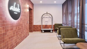 A modern waiting area with a red-tiled wall, a neon sign, a metal-framed chair, and a small table. - Abode Phillip (Phillip)