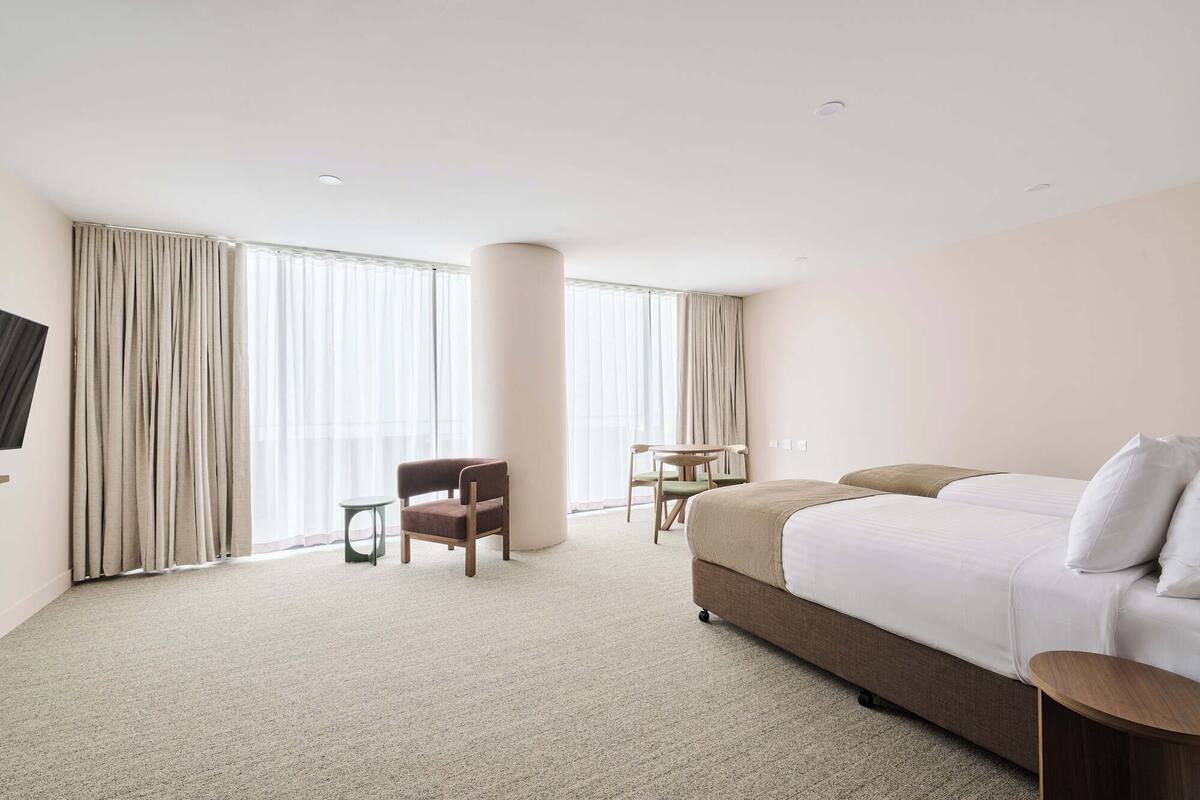 A hotel room with a large bed, a desk, two chairs, and a TV on the wall.