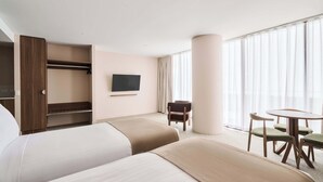 A hotel room with two beds, a TV, a chair, a table, and a large window with curtains. - Abode Phillip (Phillip)