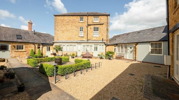 A courtyard with a central building, surrounded by stone walls and potted plants. - Immaculate 1-bed Cottage in Moreton in Marsh (Moreton-in-Marsh)
