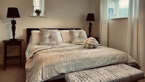 A bedroom with a bed, bedside tables, a lamp, a window with curtains, and a hanging light fixture. - Immaculate 1-bed Cottage in Moreton in Marsh (Moreton-in-Marsh)