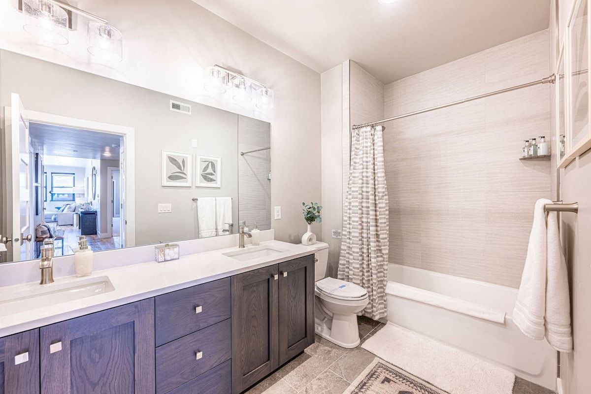 Une salle de bain avec un meuble-lavabo à deux vasques, des toilettes, une baignoire et un rideau de douche.