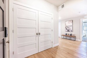 Un couloir doté d’une double porte, d’un plancher en bois et d’un banc avec des coussins.