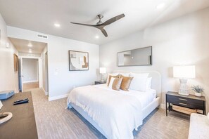 Une chambre d’hôtel comprenant un lit, des tables de chevet, un ventilateur de plafond et une porte donnant sur une autre pièce.
