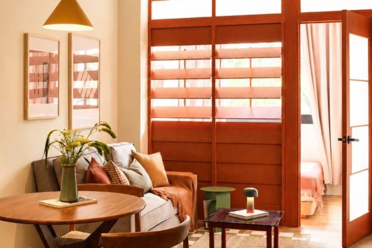 Um quarto com porta de madeira, um sofá, uma mesinha e um vaso de planta.