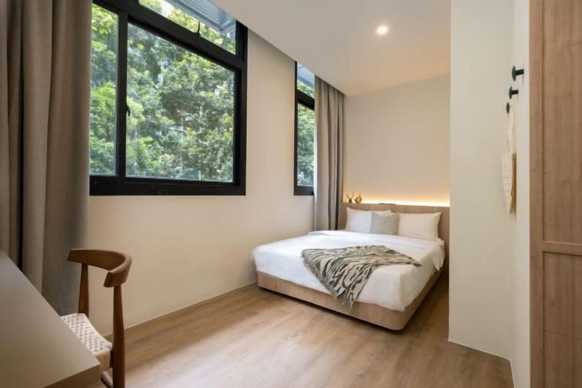 A bedroom with a bed, a chair, a window, and a bedside table.