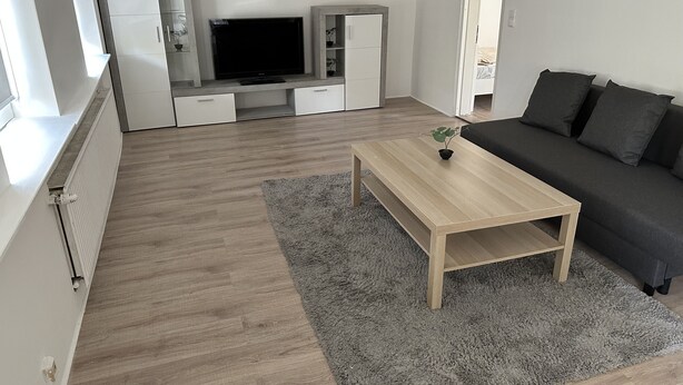 Una sala de estar moderna con una mesa de centro de madera, un sofá negro y una alfombra gris.