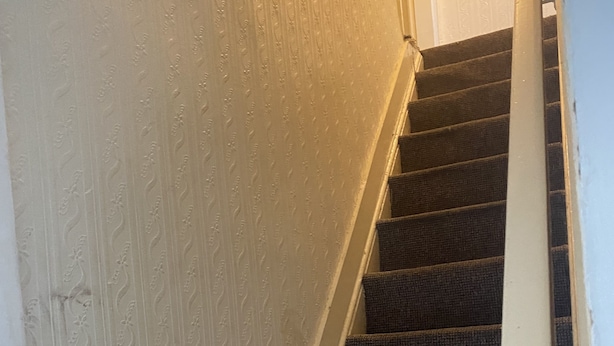 A staircase with dark carpeted steps and a white wall with a textured pattern. - Beautiful portable single room in an apartment  (Bury)