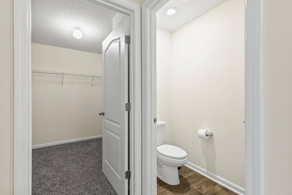 A small, clean bathroom with a toilet, a shower area, and a door leading to another room.