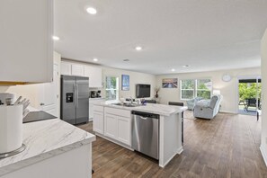 A modern kitchen with white cabinetry, a stainless steel refrigerator, and a marble countertop.