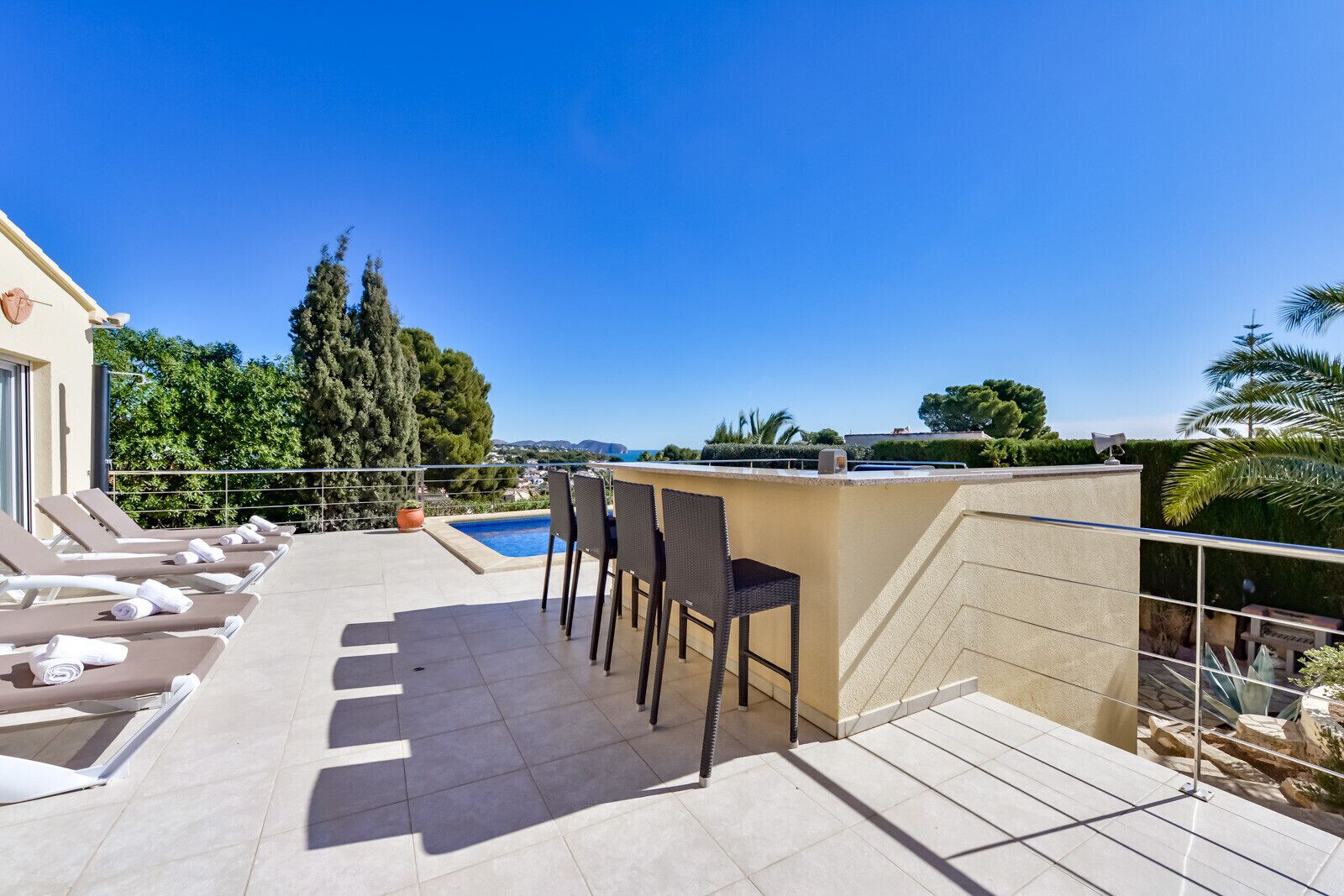 A rooftop terrace with sun loungers, a pool, and a table with chairs.