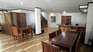 Uma sala de estar ampla com mesa e cadeiras de madeira, cozinha com armários de madeira e escada para outro andar.