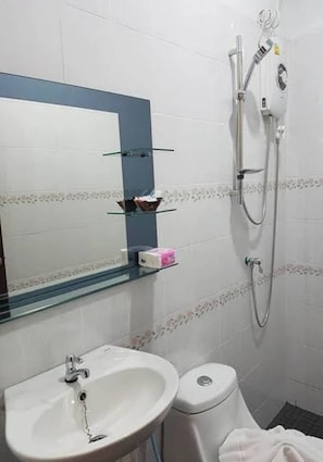A bathroom with a white sink, a toilet, a glass shelf with toiletries, and a shower with a handheld showerhead. - JP Place (Ko Lanta)