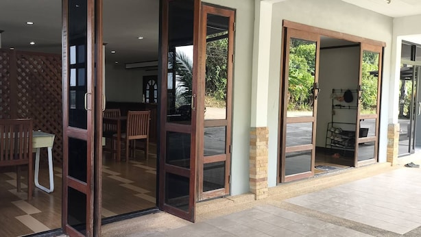 Entrada de hotel com portas de vidro abertas, piso xadrez e mesa de madeira com cadeiras.
