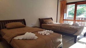 Duas camas de solteiro com roupa de cama marrom e toalhas brancas, uma janela com cortinas e vista para o verde lá fora.