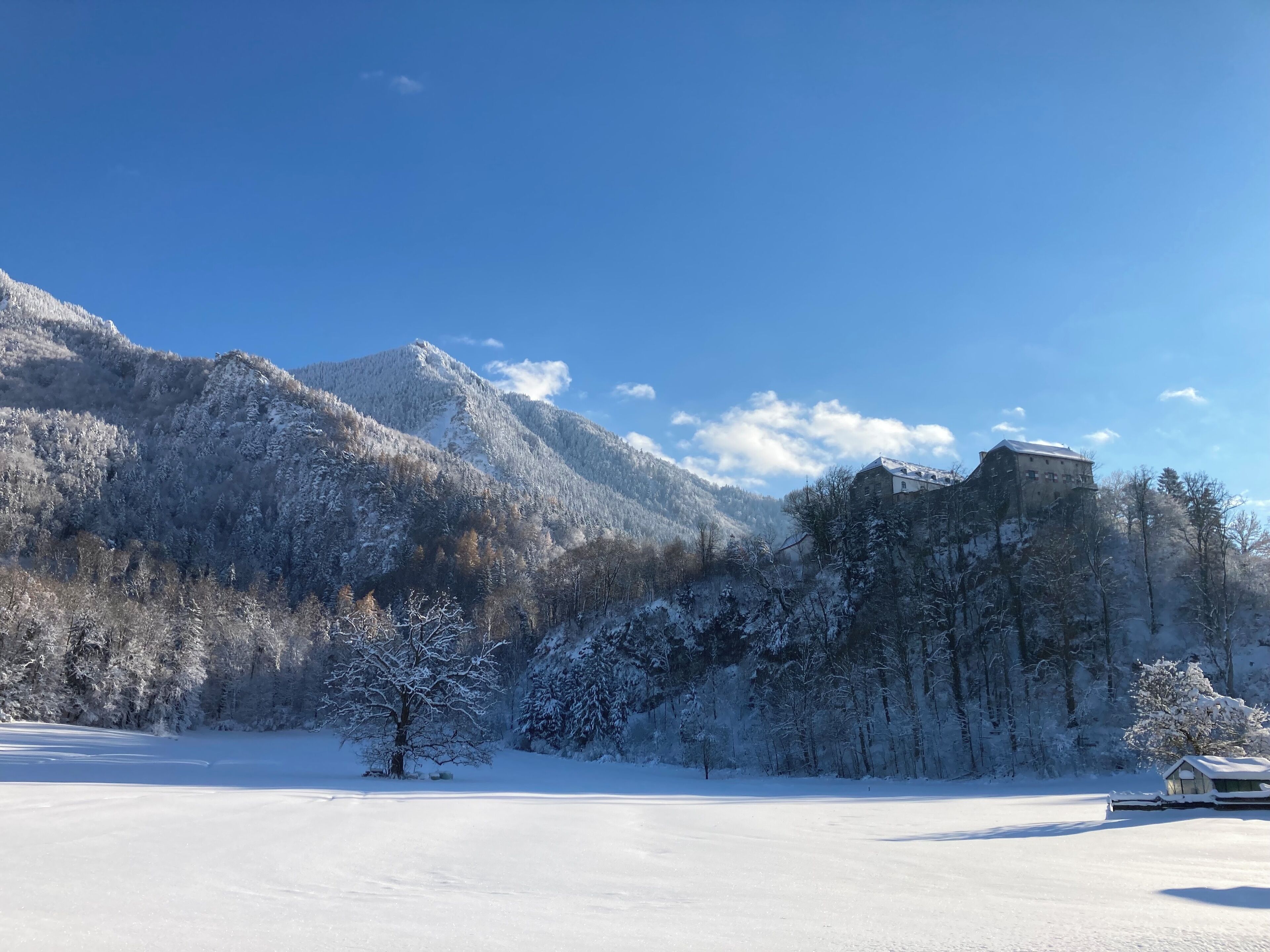 A snow-covered landscape with a mountain, a building on a hill, and a clear sky.
